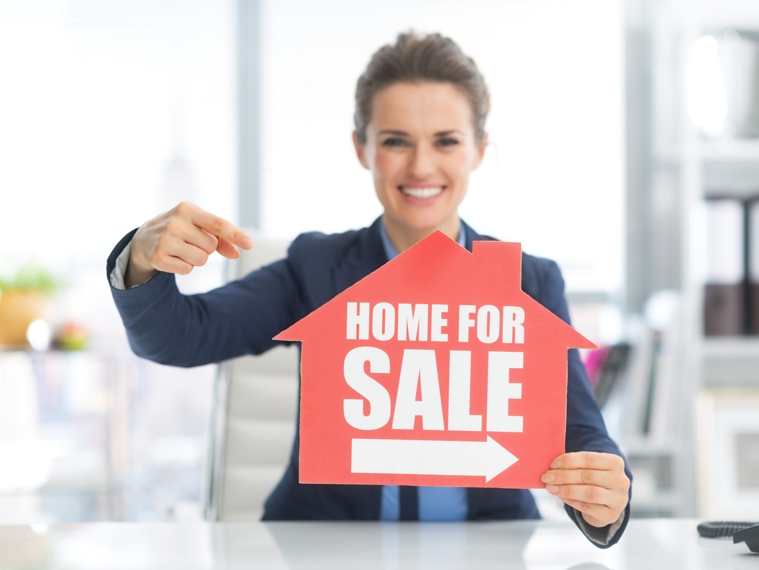 Realtor woman pointing to home for sale sign she is holding